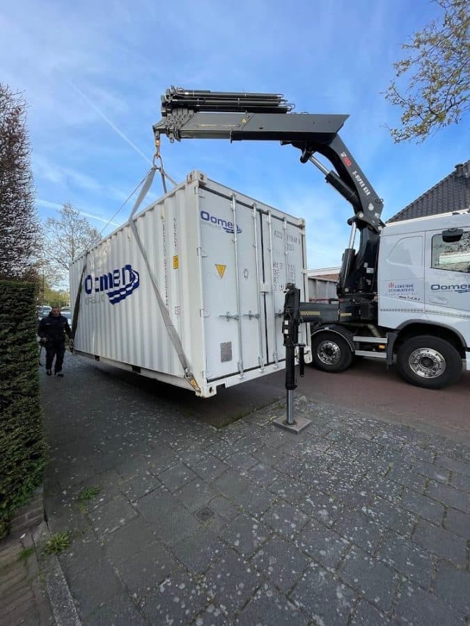 Mobiele opslagcontainer van Oomen wordt met een autolaadkraan in een woonstraat geplaatst