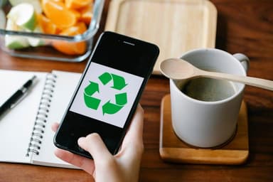 Smartphone met recyclingsymbool op een bureau met notitieboek en koffiemok
