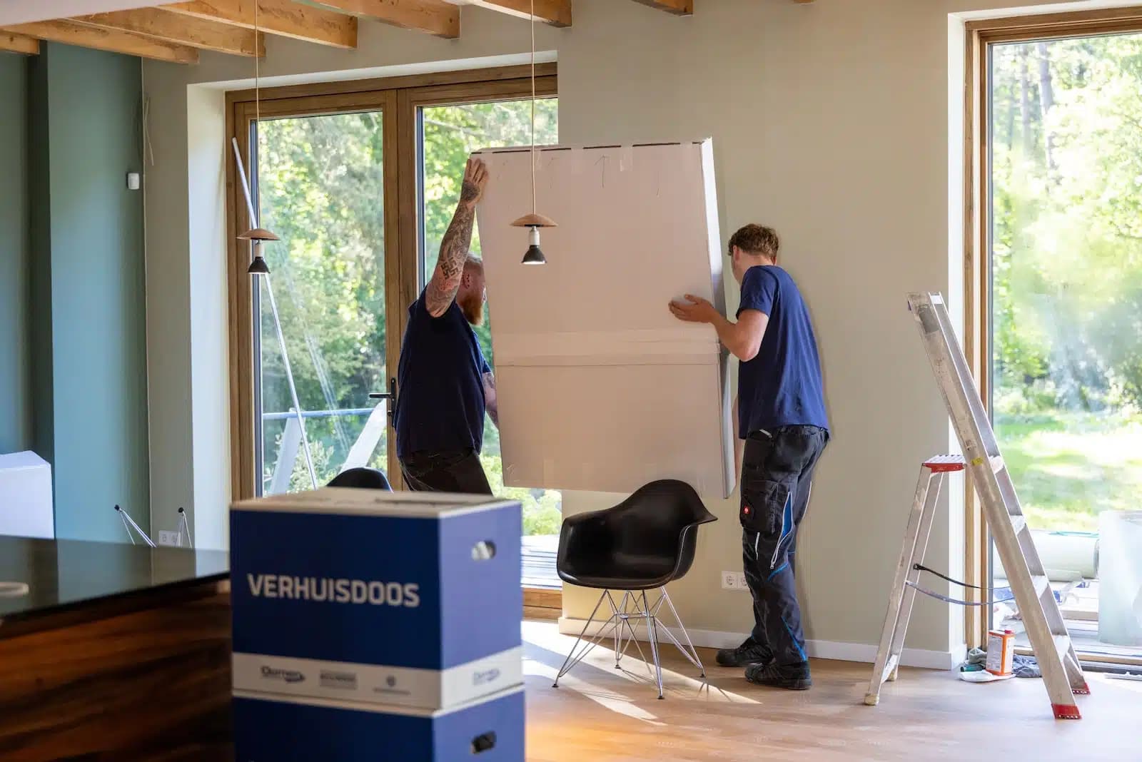 Twee verhuizers van Oomen tillen samen een groot wit paneel in de woonkamer