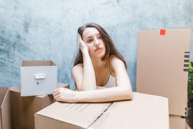 Vrouw leunt peinzend op een verhuisdoos tussen ingepakte dozen