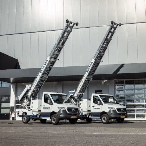 Two Oomen moving lift trucks with extended ladder lifts in front of the company premises