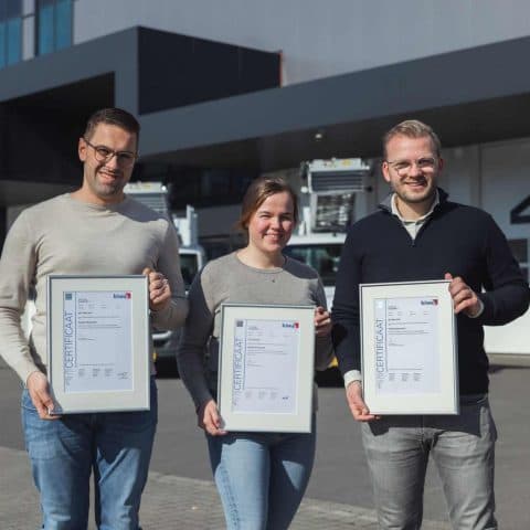 Three Oomen employees presenting their ISO certificates in front of the company premises