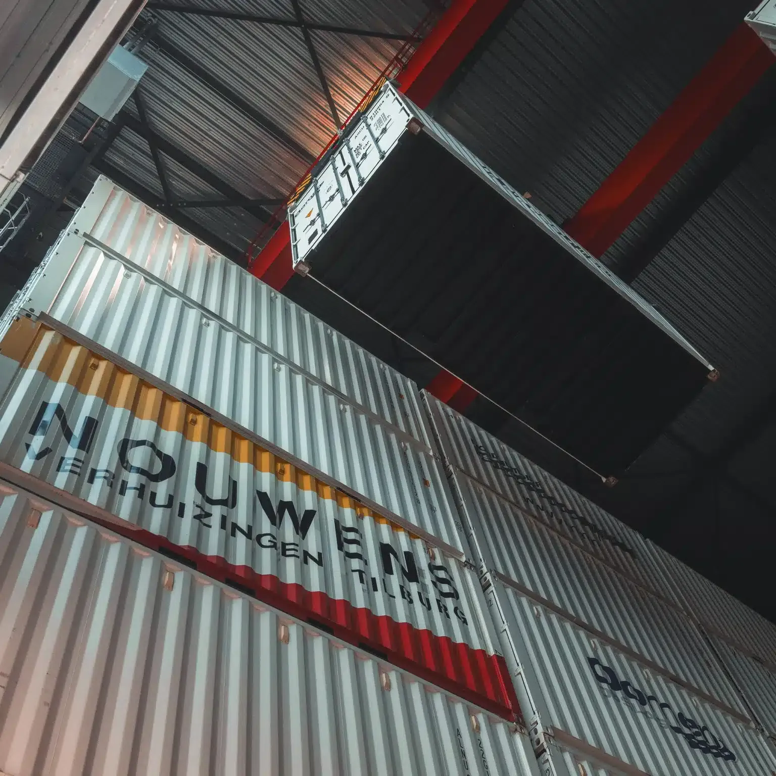 Kraan tilt een opslagcontainer in de opslaghal in Tilburg, boven containers van Nouwens Verhuizingen