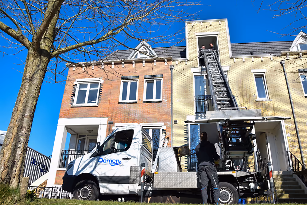 Verhuislift van Oomen tegen de gevel van een woning, met verhuizers bij het raam op de tweede verdieping